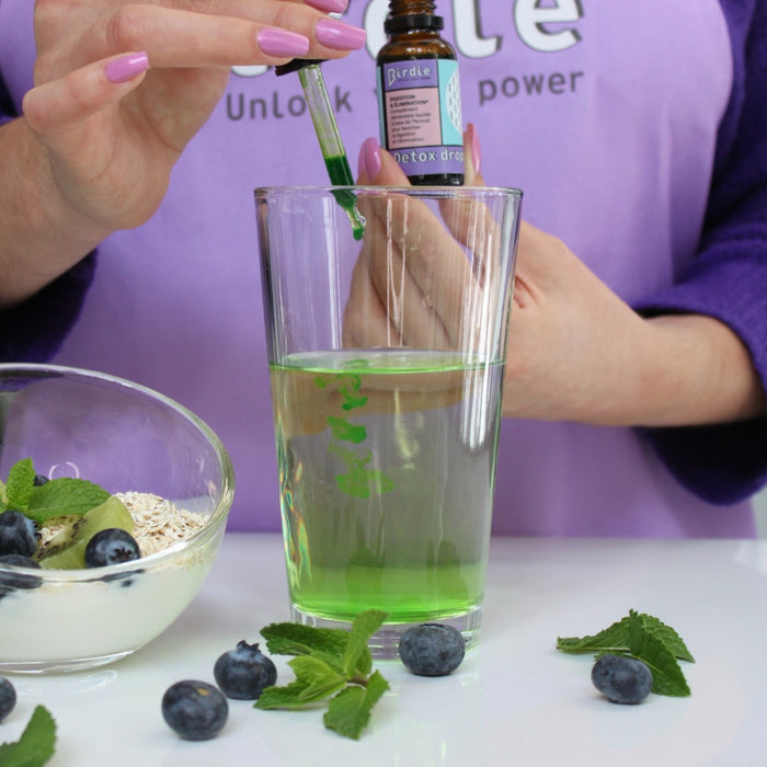 Femme prenant sa cure Detox Drops dans un verre d'eau