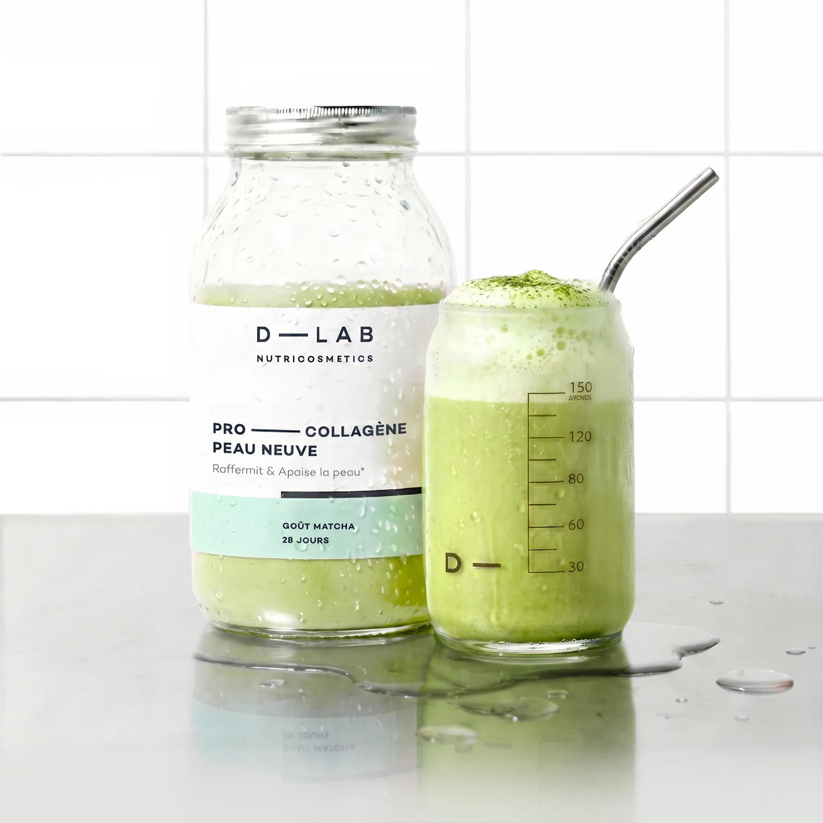 Flacon en verre Pro-Collagène Peau Neuve goût matcha D-LAB et verre de boisson verte moussée saupoudrée de matcha, paille inox, plan de travail carrelé blanc