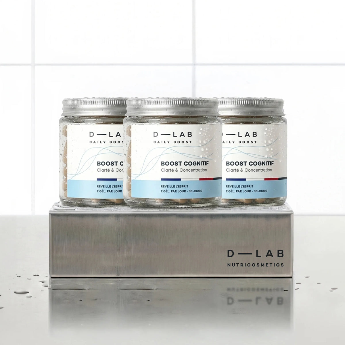 Boost Cognitif Daily Boost D-LAB Nutricosmetics, cure 3 mois : 3 flacons de gélules alignés sur un socle inox brossé, fond carrelage blanc